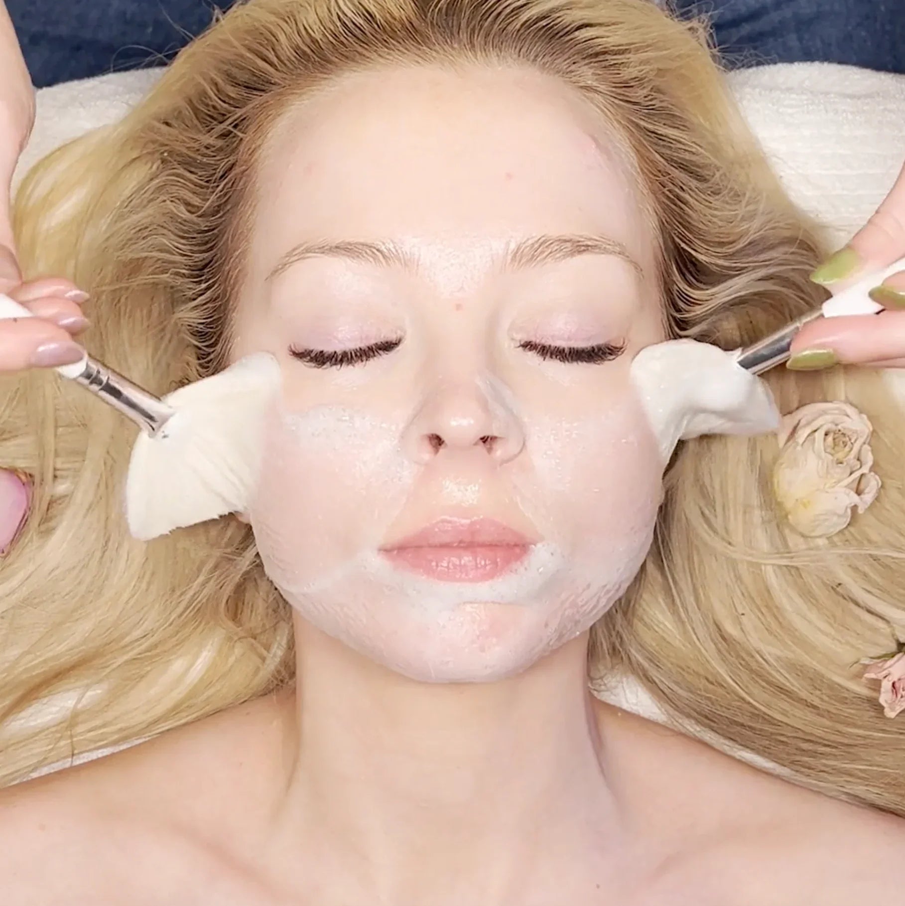 Woman receiving Bohemia Skin holistic facial treatment with soft brushes and cream mask.