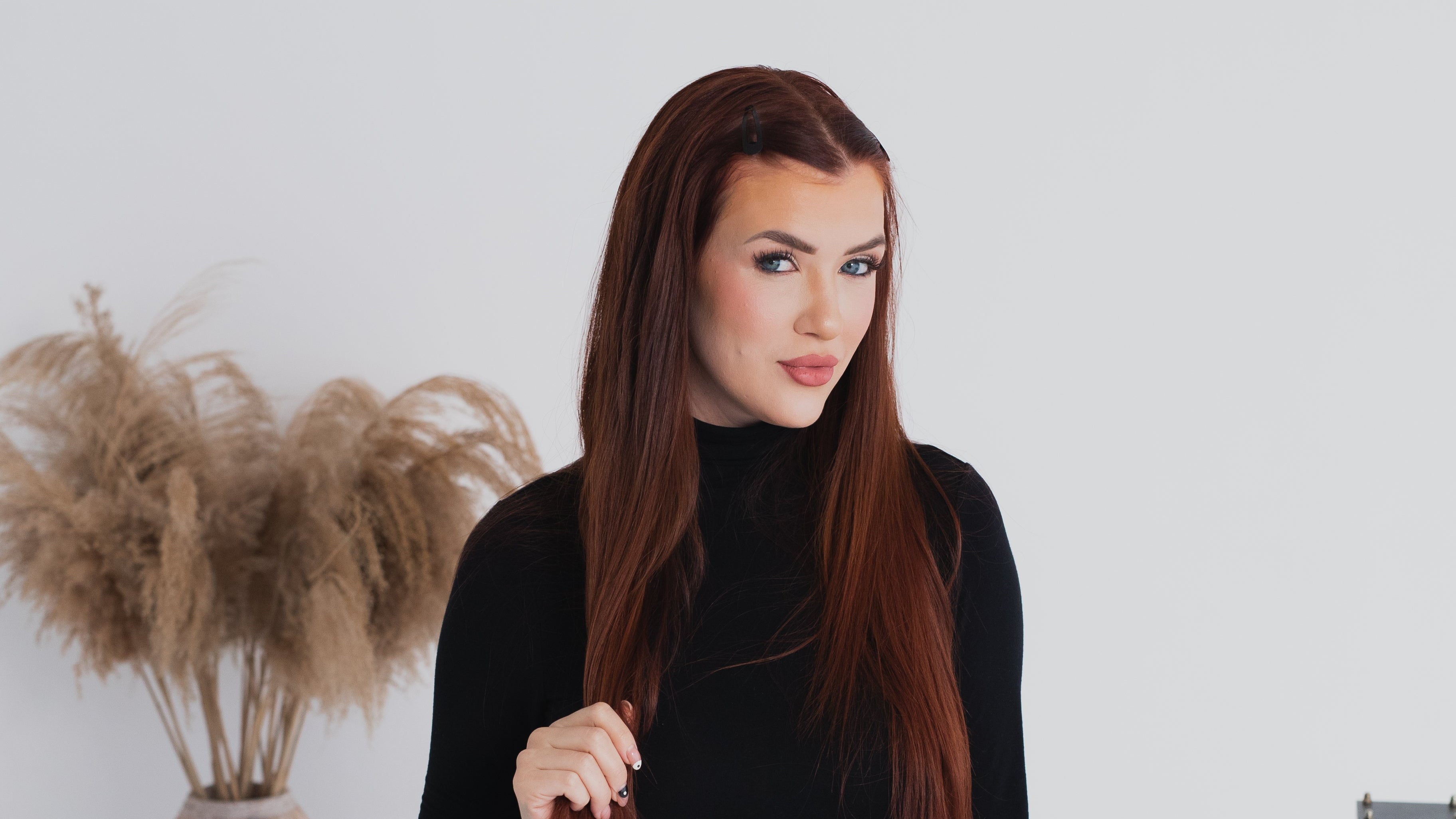 Woman in a black outfit standing in a minimalistic room with plants and a white wall.