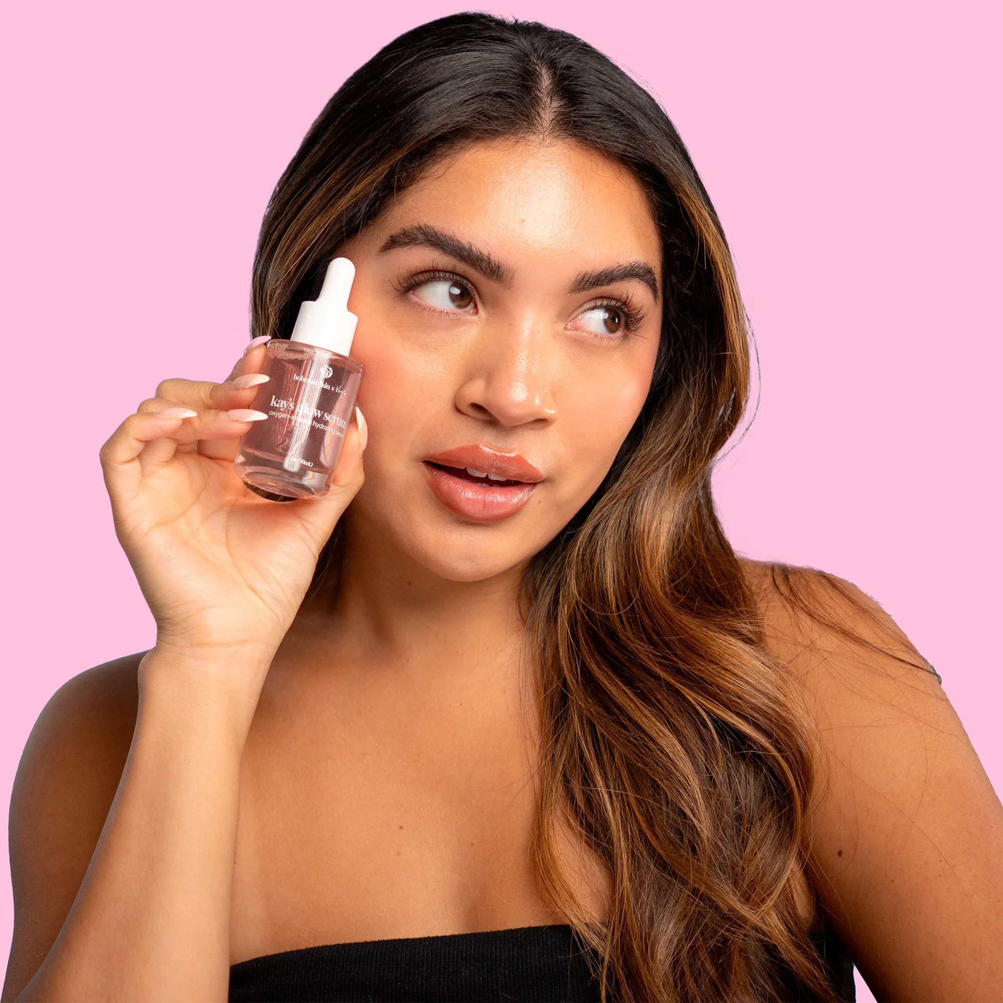 Woman holding Bohemia Skin serum bottle against pink background, showcasing clean skincare